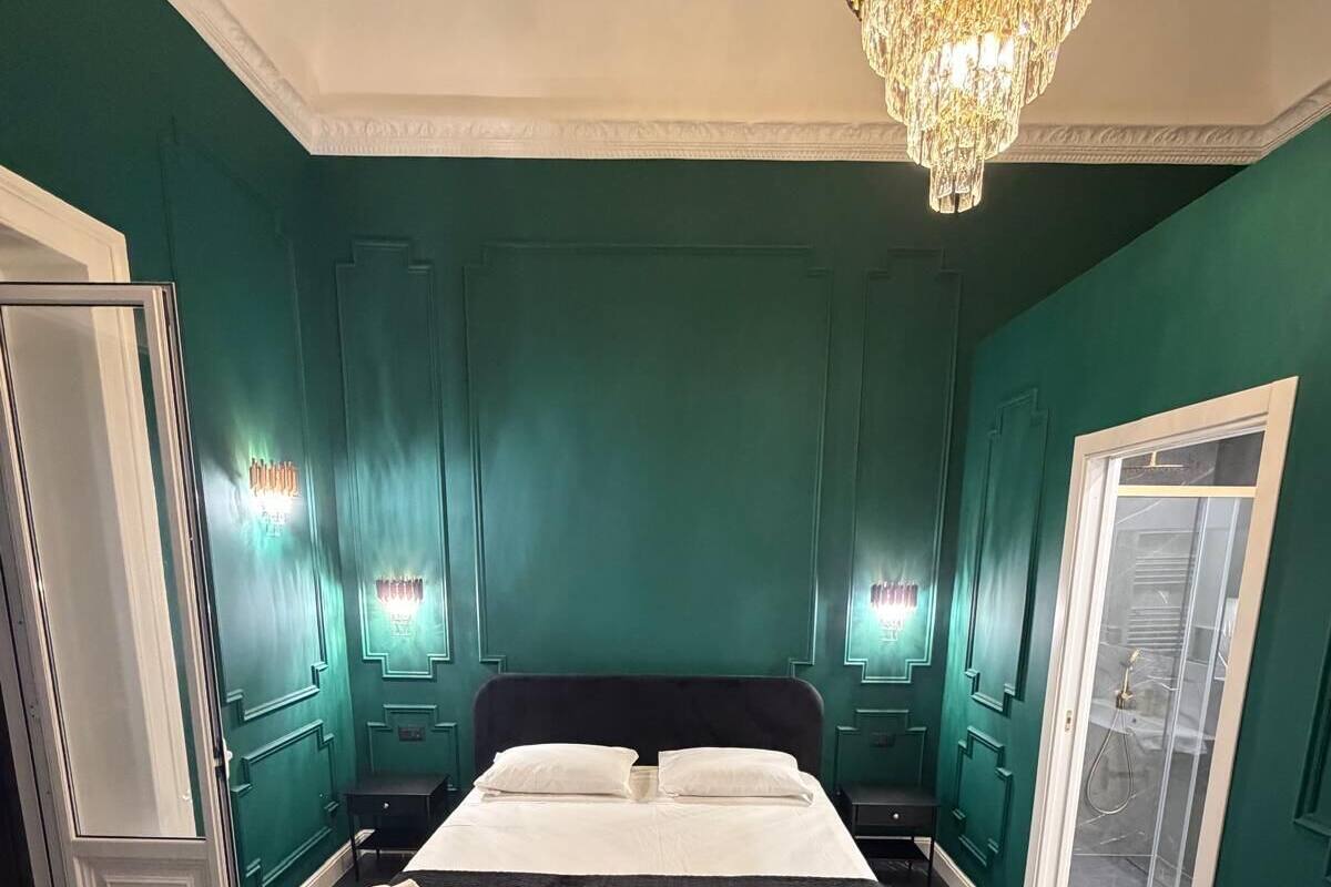 A spacious bedroom with a large bed, a chandelier, and a sliding glass door leading to a balcony.