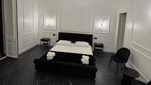 Un dormitorio moderno con una cama grande, un banco tapizado negro, una silla negra y una lámpara colgante dorada.