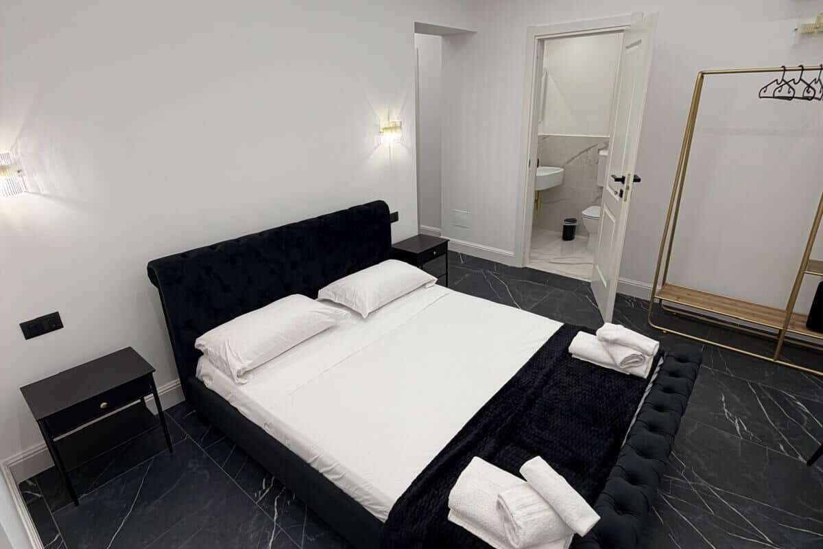 A modern bedroom with a large bed, a bedside table, a black rug, and a mirror.