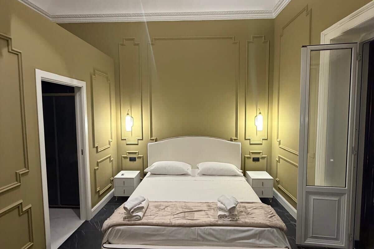 A hotel room with a large bed, two bedside tables, a ceiling fan, and a mirror.