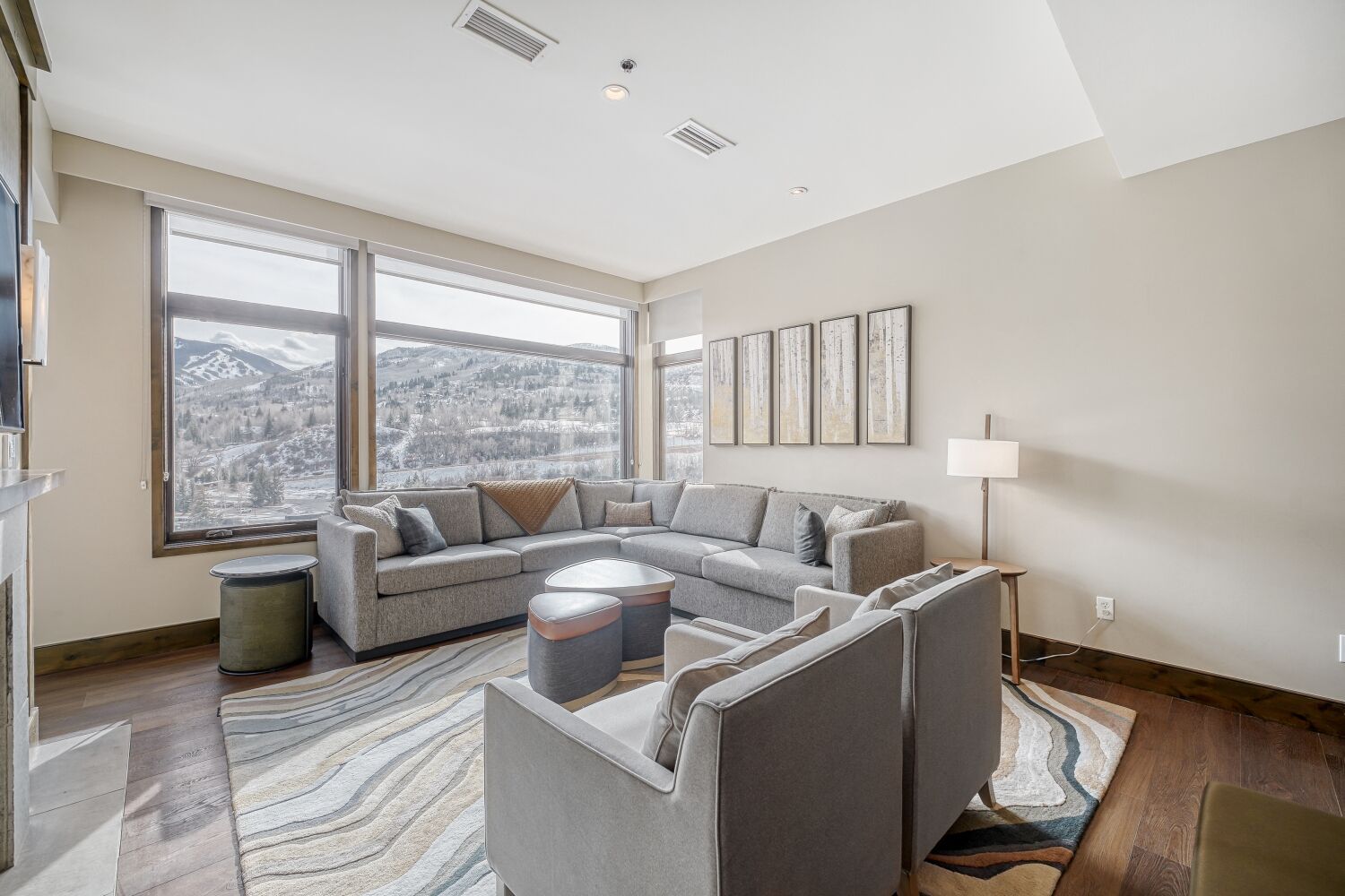 Een moderne woonkamer met een grote modulaire bank, een ronde salontafel en uitzicht op een besneeuwd berglandschap door grote ramen.