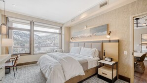 A modern hotel room with a large bed, a desk, and a chair. There is a large window with a view of mountains. - Charlie's Slopeside: Riverfront Resort/Spa, Ski-In/Out, Private Deck, Mountain Views, Remodeled #821 (Avon)