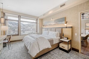 A modern hotel room with a large bed, a desk, and a chair. There is a large window with a view of mountains. - 2BR ski-in/out condo with mountain and pool views in Avon. (Avon)