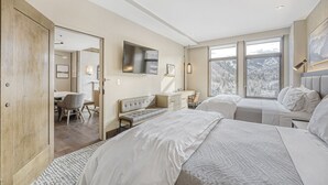A modern hotel room with a large bed, a desk, and a view of a snowy mountain. - 2BR ski-in/out condo with mountain and pool views in Avon. (Avon)