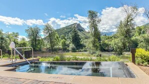 A pool with a metal railing, surrounded by greenery and a mountain in the background. - Charlie's Slopeside: Riverfront Resort/Spa, Ski-In/Out, Private Deck, Mountain Views, Remodeled #821 (Avon)