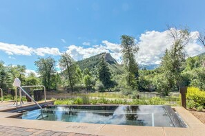 A pool with a metal railing, surrounded by greenery and a mountain in the background. - 2BR ski-in/out condo with mountain and pool views in Avon. (Avon)