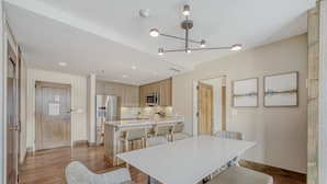 A modern kitchen with a central island, stainless steel appliances, and a dining area with a large table and chairs. - Charlie's Slopeside: Riverfront Resort/Spa, Ski-In/Out, Private Deck, Mountain Views, Remodeled #821 (Avon)