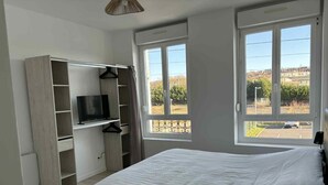 Ein Schlafzimmer mit einem Bett, einem Fernseher auf einer Holzablage und großen Fenstern mit Blick nach draußen.