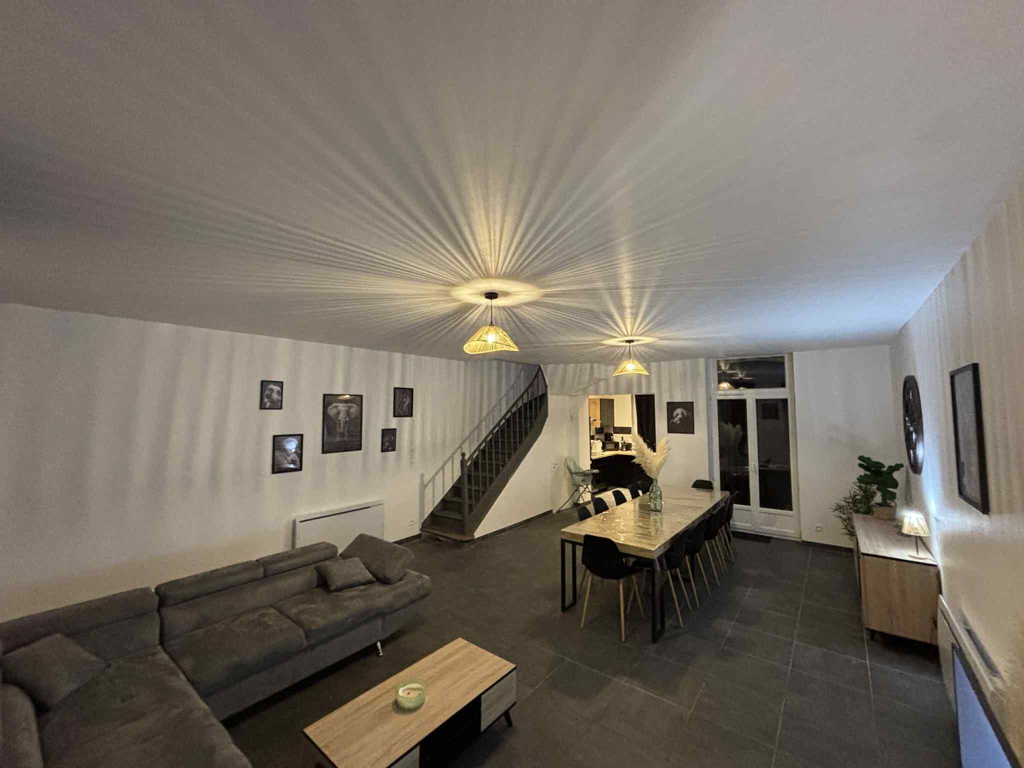 A modern living room with a sofa, coffee table, and dining area with chairs. There is a staircase leading to another level.