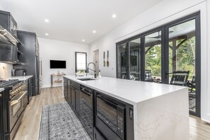 A modern kitchen with a large island, black cabinetry, and a view to an outdoor patio. - Stunning Family Friendly House in Dubuque, Iowa (Dubuque)