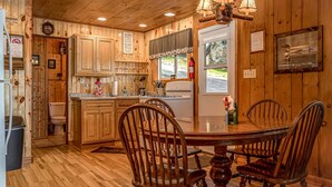 A wooden cabin-style kitchen with a dining table and chairs, wooden cabinets, a chandelier, and a fire extinguisher. - Timbers - Bouchard Shores Resort (Minocqua)