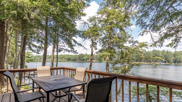 A wooden deck with a table and chairs overlooking a lake, surrounded by tall trees. - Timbers - Bouchard Shores Resort (Minocqua)