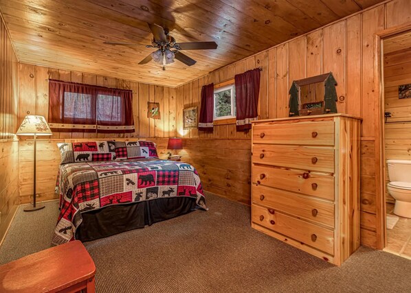 A wooden cabin bedroom with a bed, dresser, and ceiling fan. - Timbers - Bouchard Shores Resort (Minocqua)