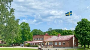 A historic building with a Swedish flag, featuring a traditional design with a red roof and brick walls. - Brevensgården (Brevens Bruk)