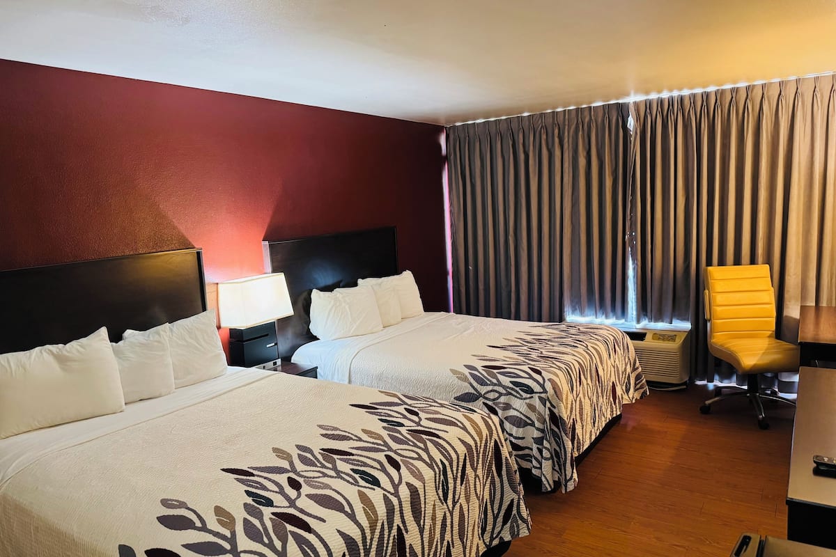 Ein Hotelzimmer mit zwei Betten, einem Nachttisch mit Lampe, einem Sessel und einem Heizkörper.