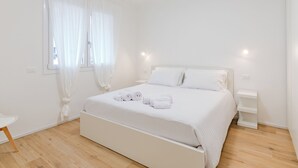 A minimalist bedroom with a bed, bedside tables, and a window with sheer curtains. - GINO SUITES - Bilocali Luxury - Appartamenti vicini a Rho Fiera e Milano (Bollate)