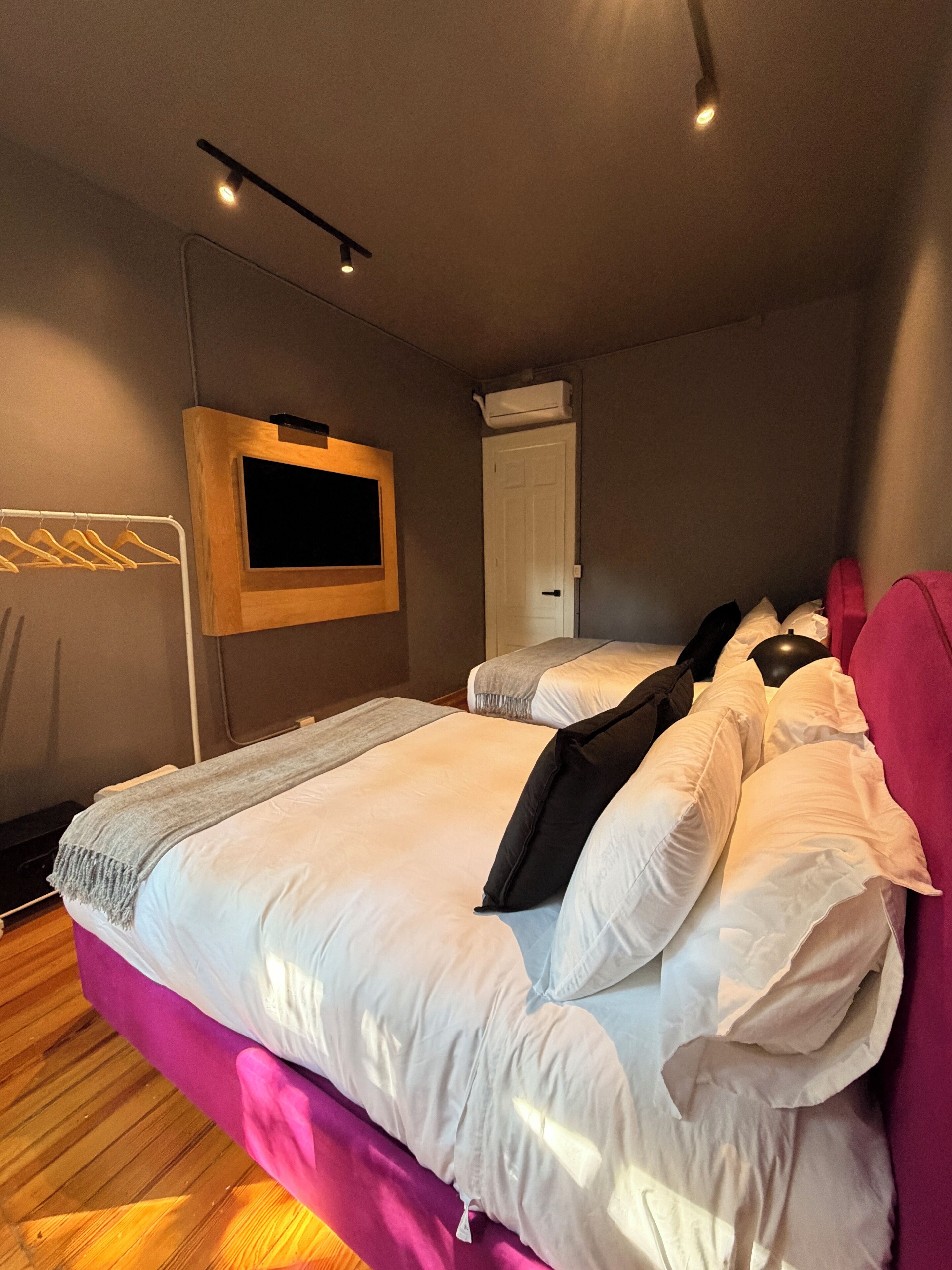 A hotel room with a large bed, a TV mounted on the wall, and a door with an air conditioning unit.