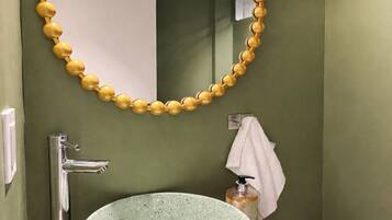 A bathroom with a round sink, a mirror with a yellow bead frame, a towel, and a soap dispenser.