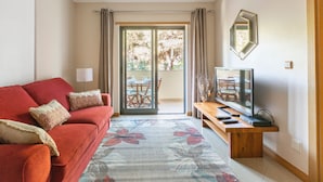 A living room with a red sofa, a flat-screen TV, and a sliding glass door leading to a balcony. - Solmar Garden View Apartment: Pool, Wi-Fi & Air Conditioning (Albufeira)