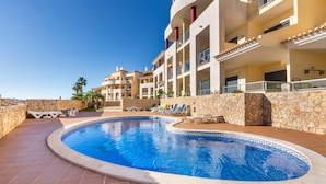 A swimming pool with a tiled edge, lounge chairs, and a stone wall. - Solmar Garden View Apartment: Pool, Wi-Fi & Air Conditioning (Albufeira)
