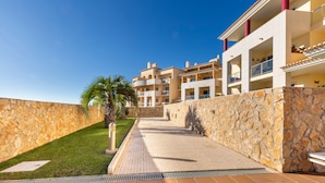 A multi-story hotel with a stone wall, tiled walkway, and a palm tree. - Solmar Garden View Apartment: Pool, Wi-Fi & Air Conditioning (Albufeira)