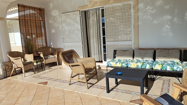 Un patio ensoleillé, aménagé avec des meubles en osier, un canapé confortable et un sol carrelé.
