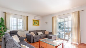 Un salon avec un canapé gris, une table basse en verre, une plante en pot et une vue à travers une porte vitrée.
