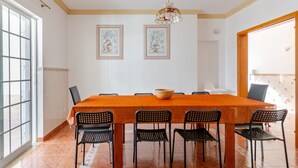 Un espace repas comprenant une longue table, six chaises, un grand saladier au centre et deux œuvres d’art encadrées accrochées au mur.