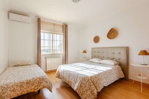 Een slaapkamer met een bed, twee nachtkastjes, een raam met gordijnen en een airconditioning.