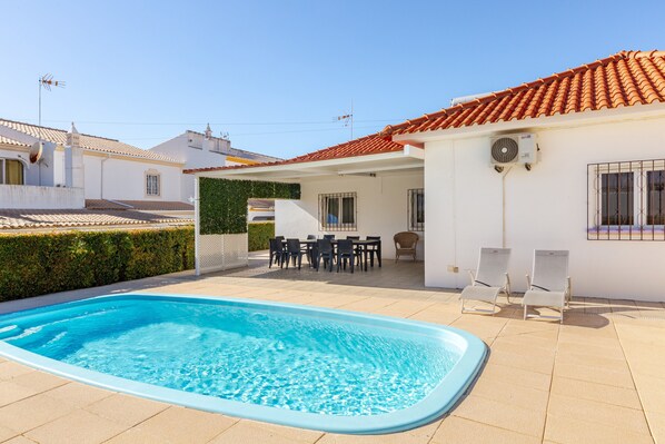 A swimming pool with lounge chairs, a patio area with tables and chairs, and a white building with a red-tiled roof. - Villa Claramar: Private Pool, Wi-Fi and Air Conditioning in Albufeira (Albufeira)
