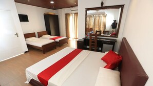 A hotel room with a large bed, two smaller beds, a desk, and a mirror. - pavona lake hotel (Sigiriya)