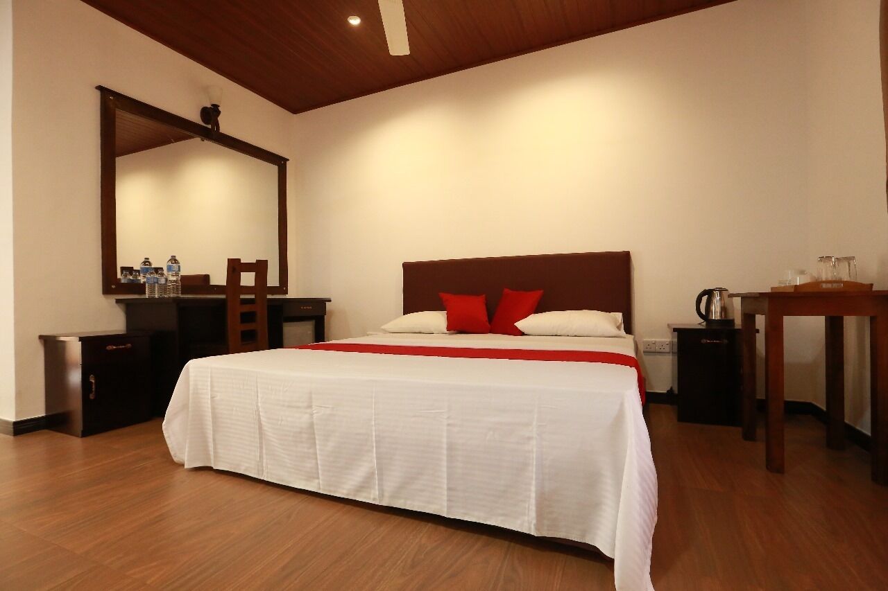 Habitación de hotel con una cama grande, cabecera de madera, mesita de noche, espejo y una pequeña mesa con un hervidor.