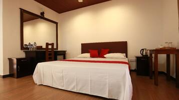 Habitación de hotel con una cama grande, cabecera de madera, mesita de noche, espejo y una pequeña mesa con un hervidor.