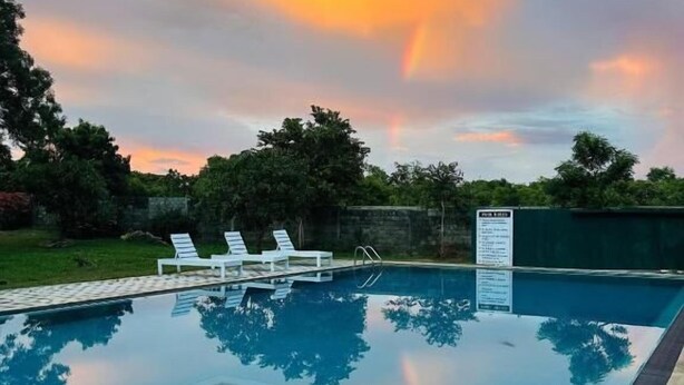 A swimming pool with lounge chairs and a sign, surrounded by greenery. - pavona lake hotel (Sigiriya)
