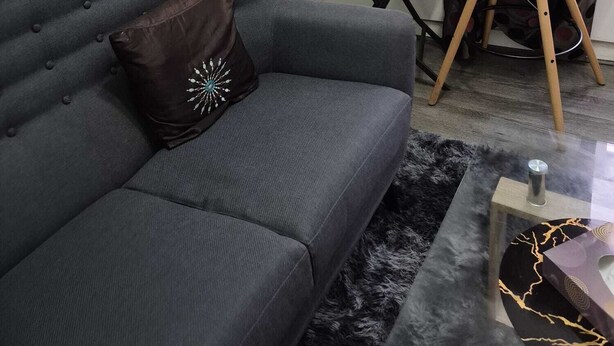 Una sala de estar moderna con un sofá gris, una pequeña mesa redonda con un florero y una silla blanca.