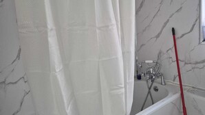 Un baño con pared de mármol blanco, una bañera blanca y una escoba roja apoyada en la pared.