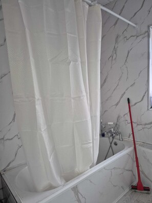 A bathroom with a white marble wall, a white bathtub, and a red broom leaning against the wall. - Modern 2‑Bedroom Apartment in Moston, Manchester (Manchester)