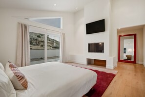 A bedroom with a large bed, a TV mounted on the wall, and a view of a natural landscape through the window. - Breakaway By Homestead Modern (Joshua Tree)