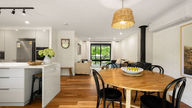 Een moderne keuken met een centraal eiland, een eethoek met een houten tafel en een groot raam met uitzicht op groen.