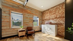 A room with wooden panel walls, a brick accent wall, a white cabinet, a brown leather chair, and a small table with a plant. - The Modern Loft at the foot of the Bighorns (Buffalo)