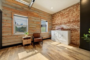 Ein Zimmer mit Holzwandverkleidung, einer Wand aus Ziegelsteinen, einem weißen Schrank, einem braunen Ledersessel und einem kleinen Tisch mit einer Pflanze.