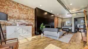 A modern living room with a brick wall, white cabinets, a grey sofa, and a dining area. - The Modern Loft at the foot of the Bighorns (Buffalo)