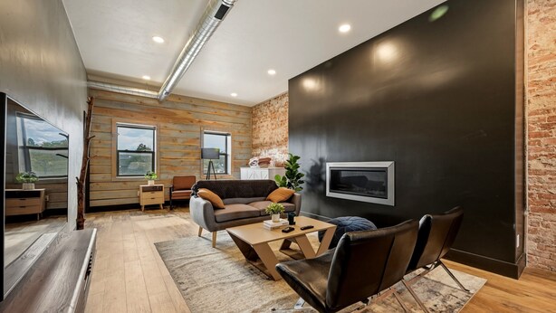 A modern living room with a sofa, coffee table, and chairs, a flat-screen TV mounted on a dark wall, and large windows with a view. - The Modern Loft at the foot of the Bighorns (Buffalo)