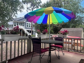 En terrasse med et bord og stole, en farverig parasol og krukker med planter.