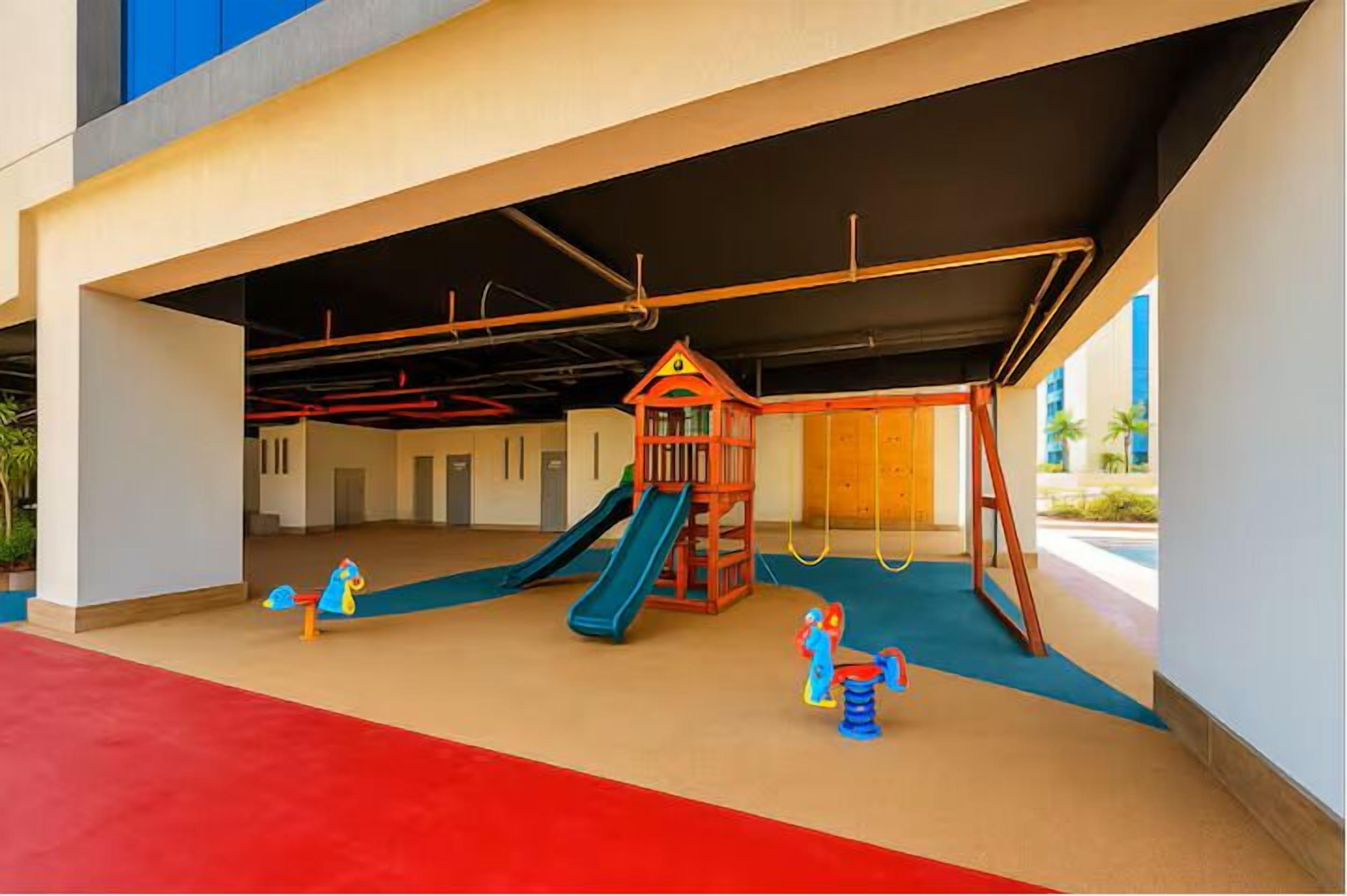 Un área de juegos infantiles con tobogán, estructura de escalada y balancín.