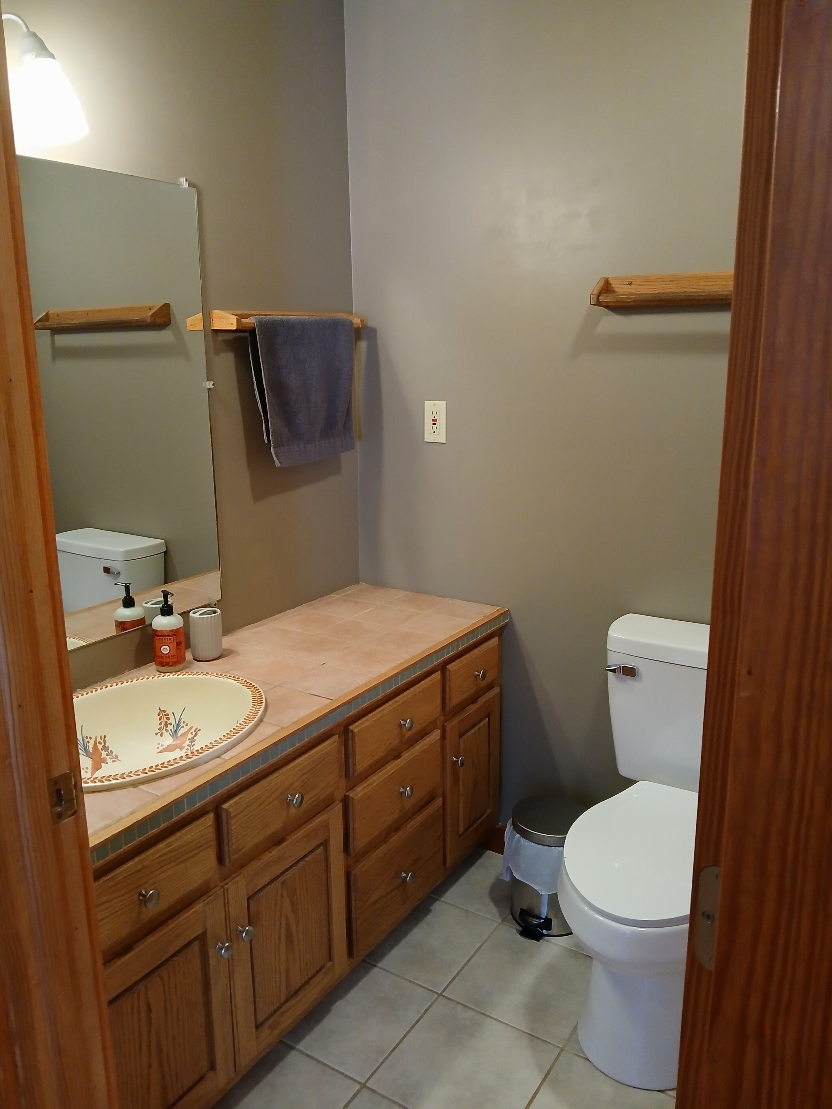 A bathroom with a wooden vanity, a sink with a decorative basin, a mirror, a toilet, and a towel hanging on a rack.