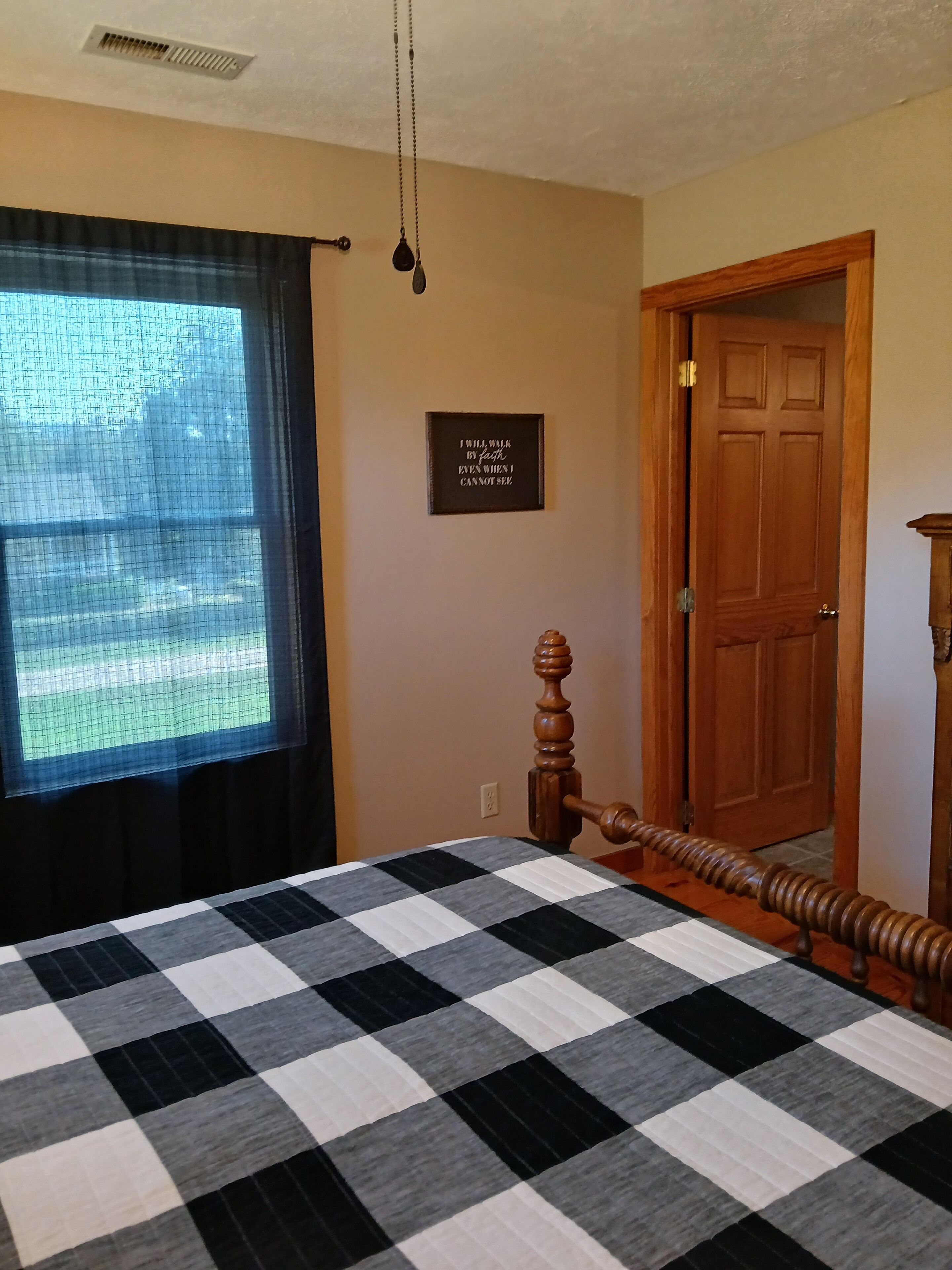 A bedroom with a checkered bedspread, a wooden door, and a wall-mounted light fixture.