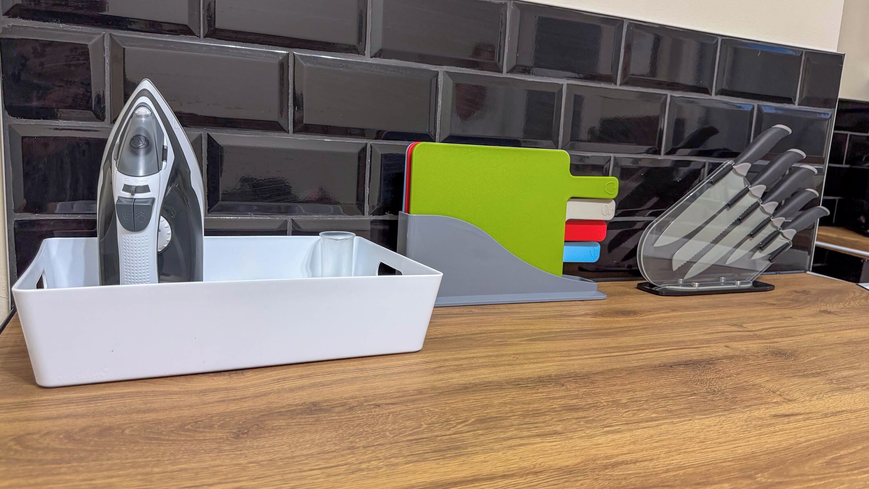 A kitchen counter with a white dish rack, a knife block, and a colorful cutting board.