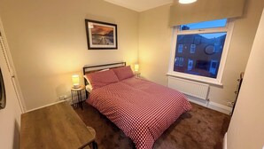 A bedroom with a bed, bedside lamps, a framed picture on the wall, a window with a view of buildings, and a radiator. - Family/business - Parking - Wifi - Sleeps 3 (Barnsley)