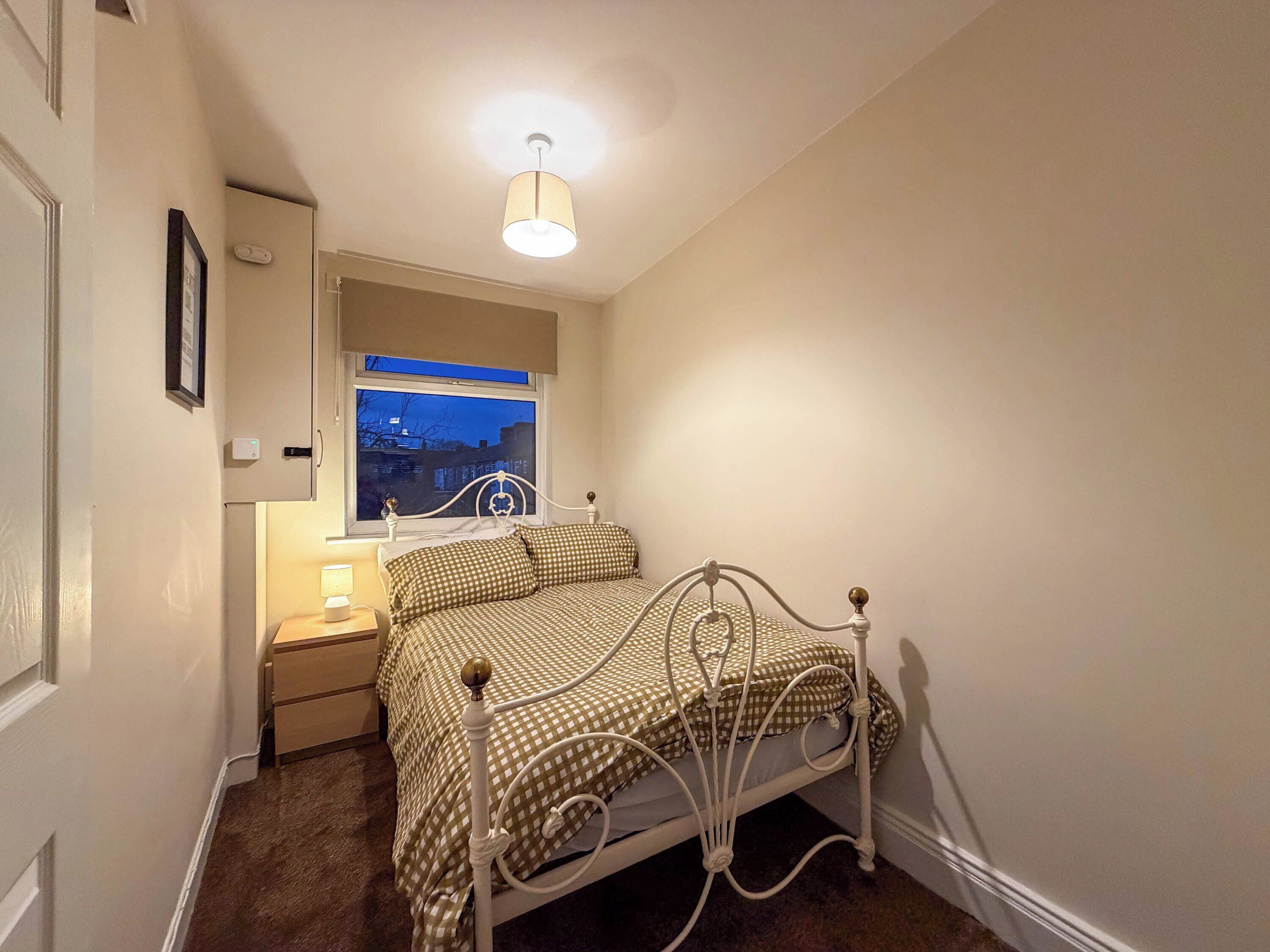 A bedroom with a bed, bedside table, lamp, and a window with a view of buildings.